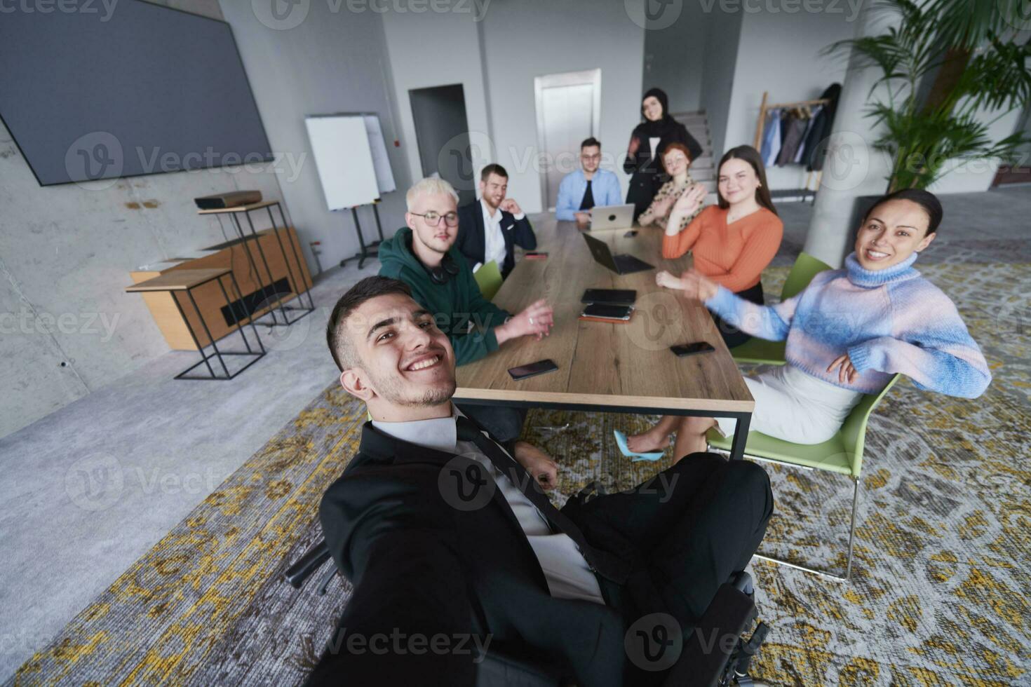 i en modern kontor, en grupp av affärsmän samlas runt om en tabell under en möte, fångande en ögonblick av kamratskap och lagarbete som de ta en selfie foto