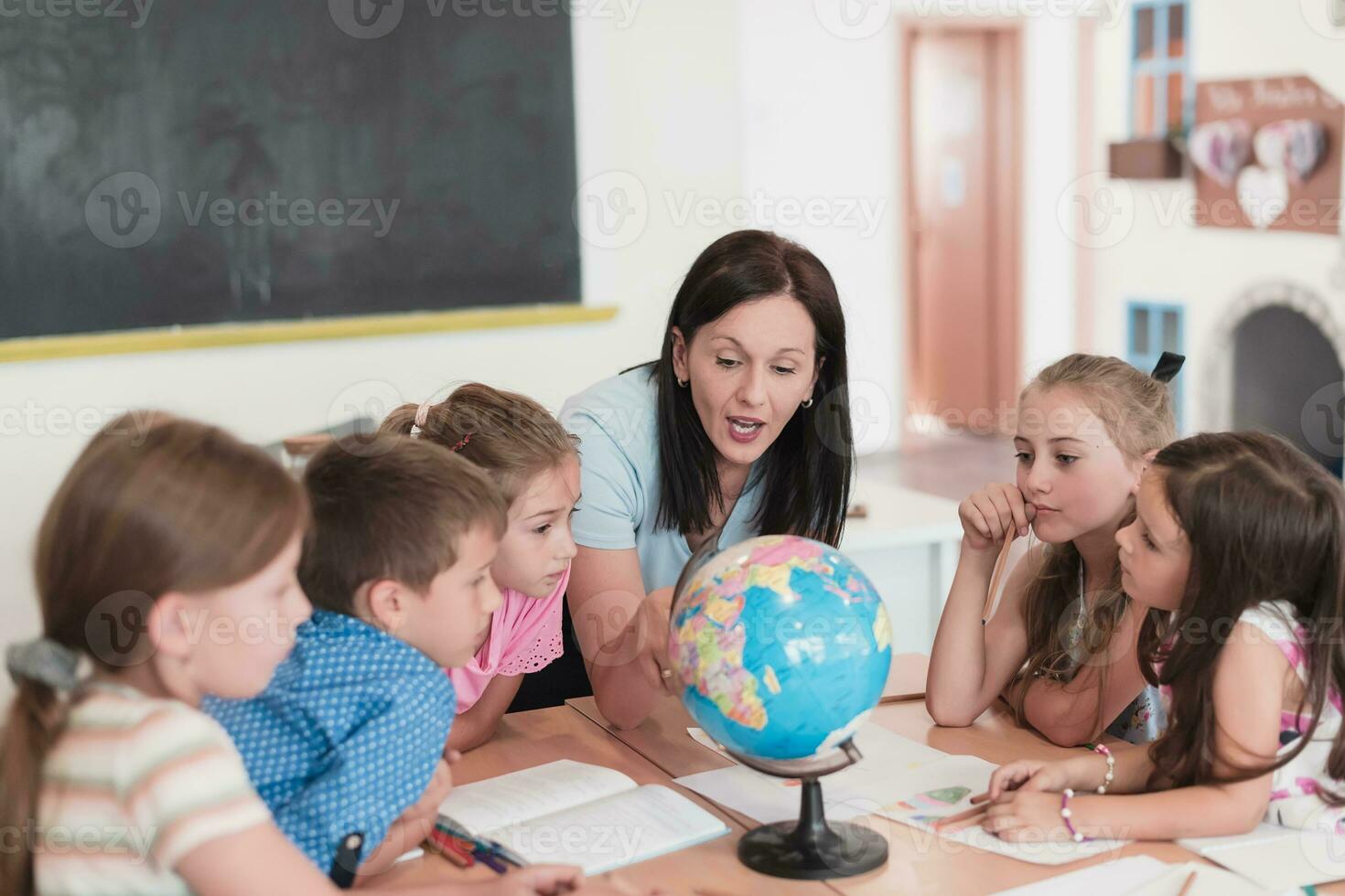 kvinna lärare med barn i geografi klass ser på klot. sida se av grupp av olika Lycklig skola barn med klot i klassrum på skola. foto