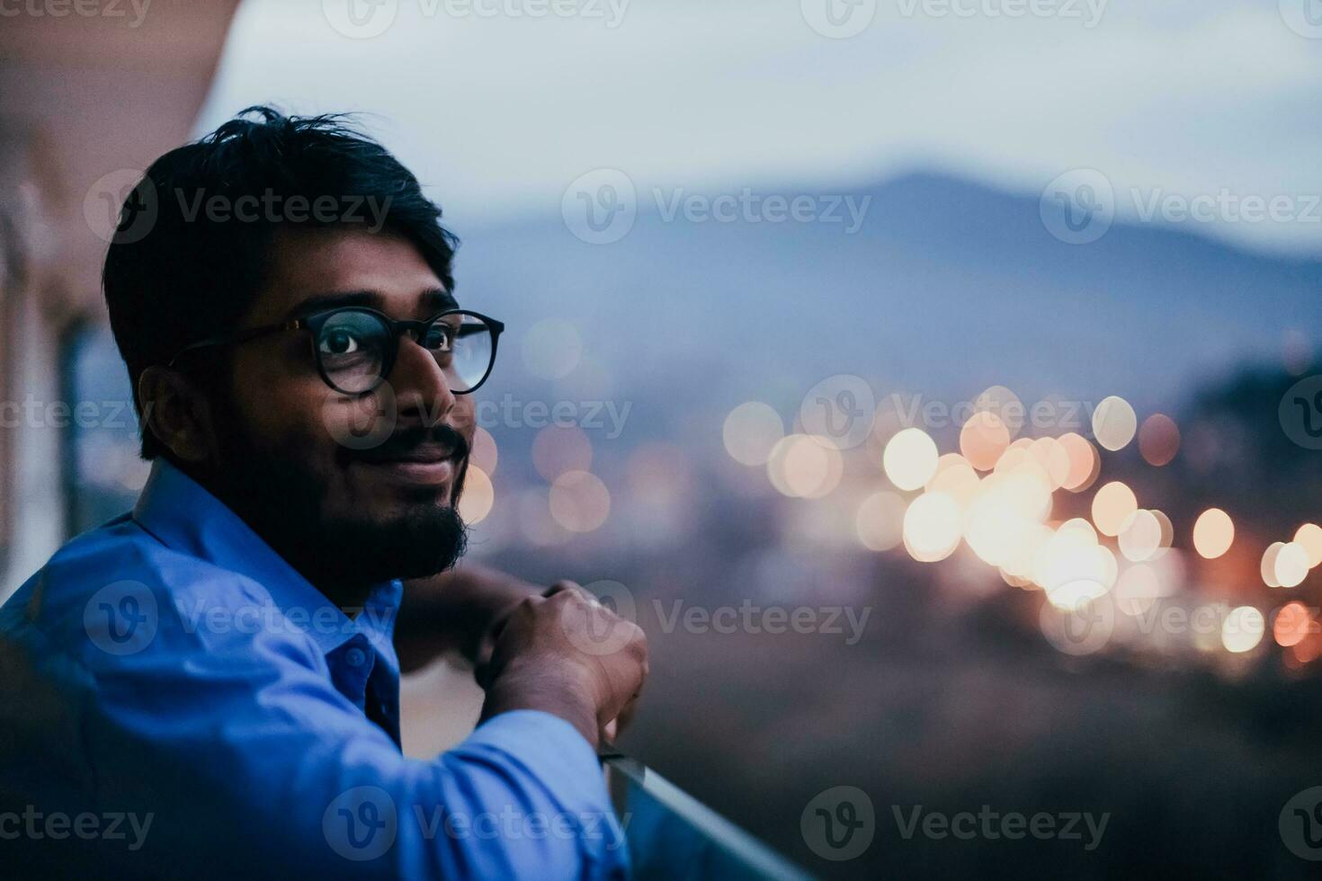 ett indisk man med glasögon och en blå skjorta utseende runt om de stad på natt. i de bakgrund av de natt gata av de stad foto