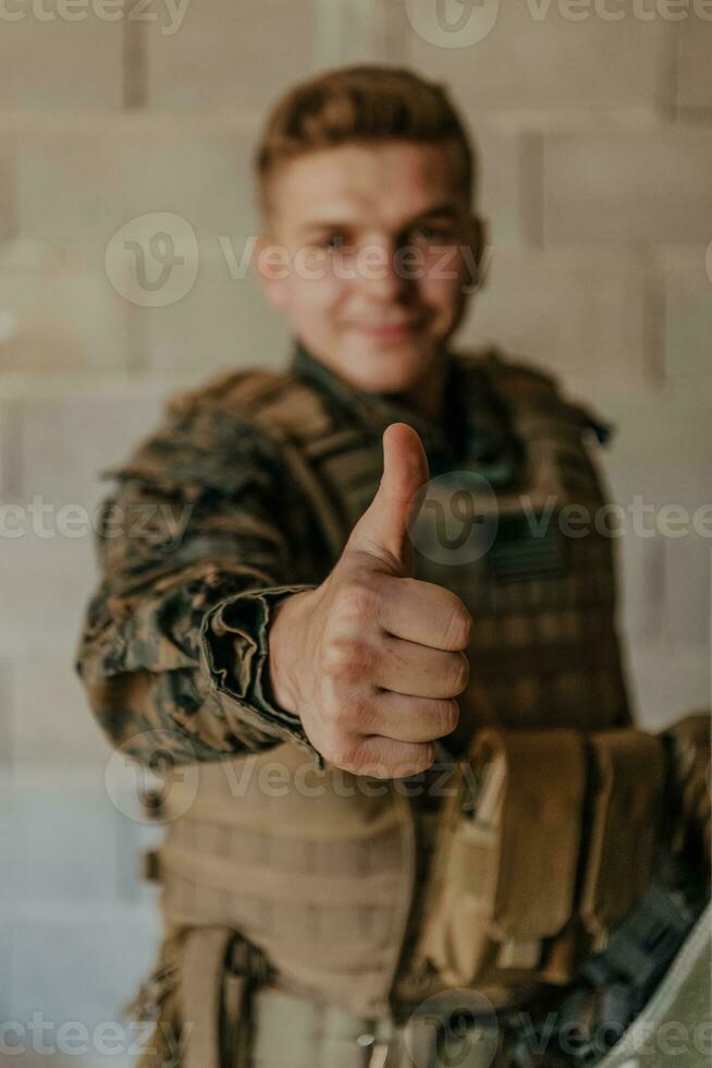 de soldat gör en gest av Framgång med hans hand. en soldat i full krig redskap står i främre av en sten vägg och visar de ok tecken med hans finger foto