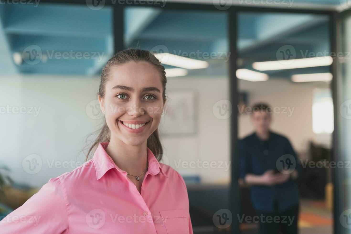 porträtt av ung leende företag kvinna i kreativ öppen Plats coworking börja kontor. framgångsrik affärskvinna stående i kontor med copyspace. medarbetare arbetssätt i bakgrund. foto