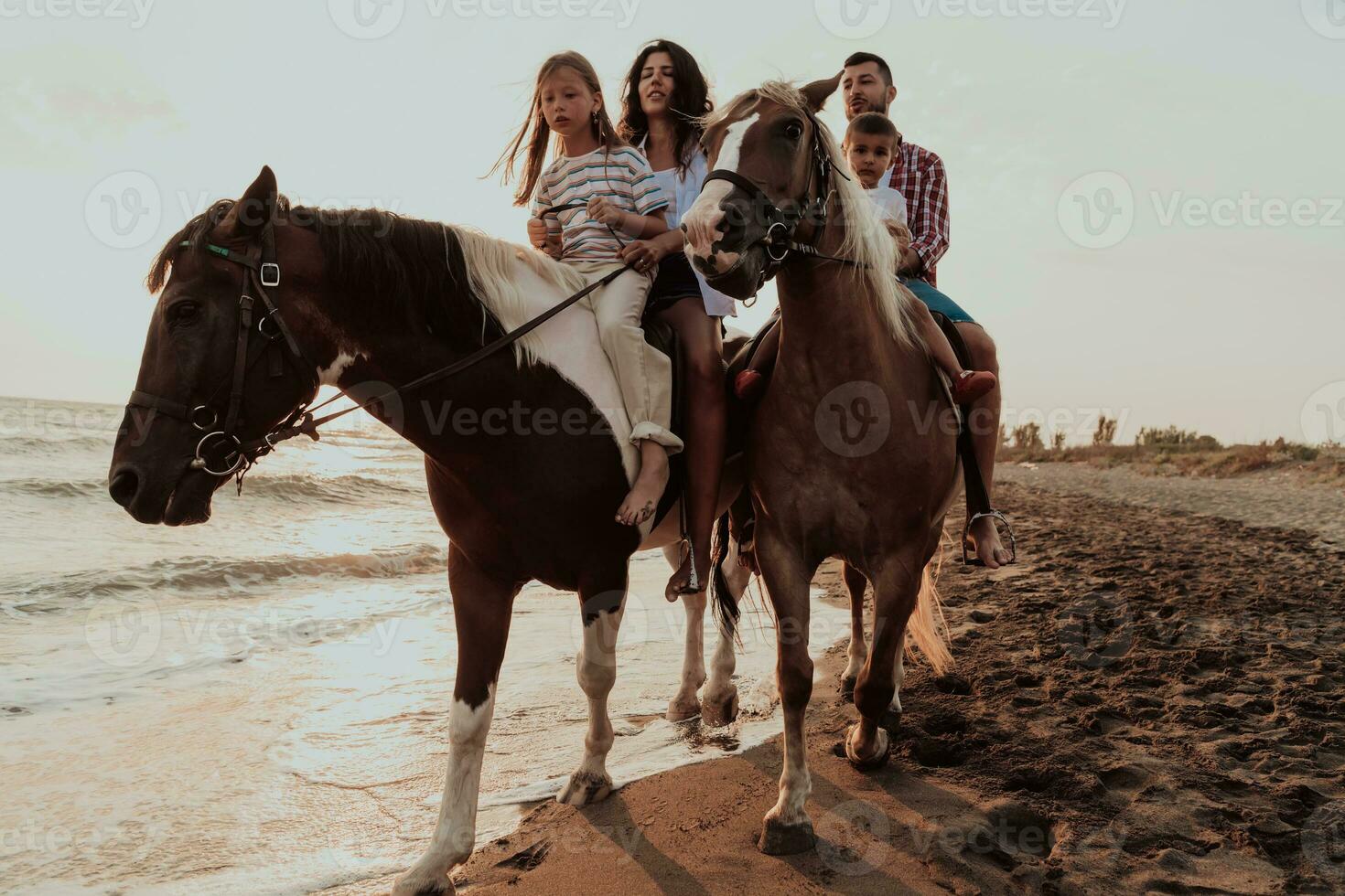 de familj spenderar tid med deras barn medan ridning hästar tillsammans på en sandig strand. selektiv fokus foto