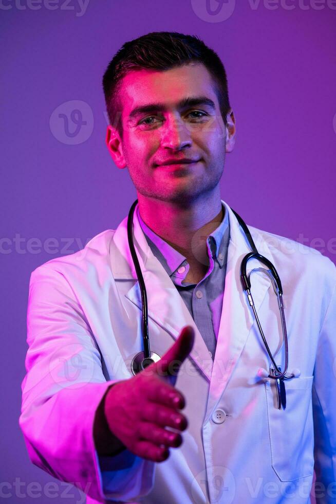 porträtt av en hjälte i en vit täcka. glad leende ung läkare med stetoskop i medicinsk sjukhus stående på blå och rosa bakgrund. varning handla om de fara av de coronavirus covid-19 foto