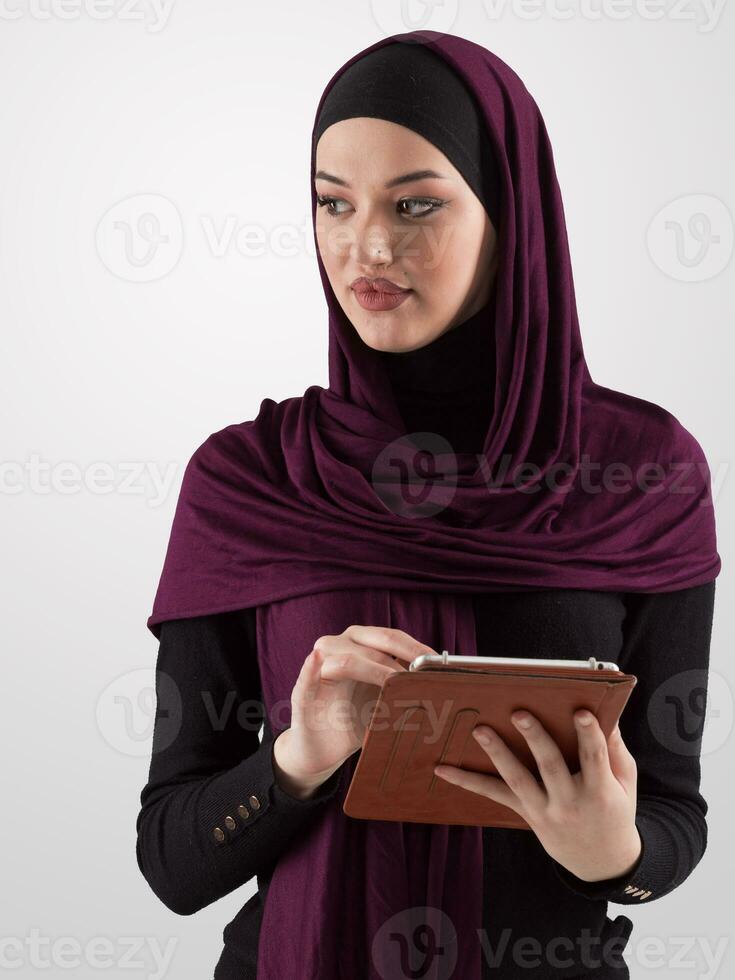 skön och modern ung arabicum affärskvinna i hijab använder sig av en läsplatta dator medan Framställ på ljus bakgrund och leende på de kamera. företag mångfald begrepp, muslim lady. foto