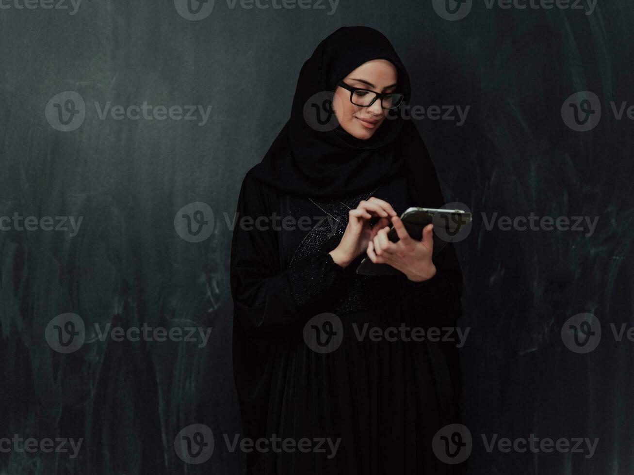 ung modern muslim företag kvinna använder sig av smartphone bär hijab kläder i främre av svart svarta tavlan foto