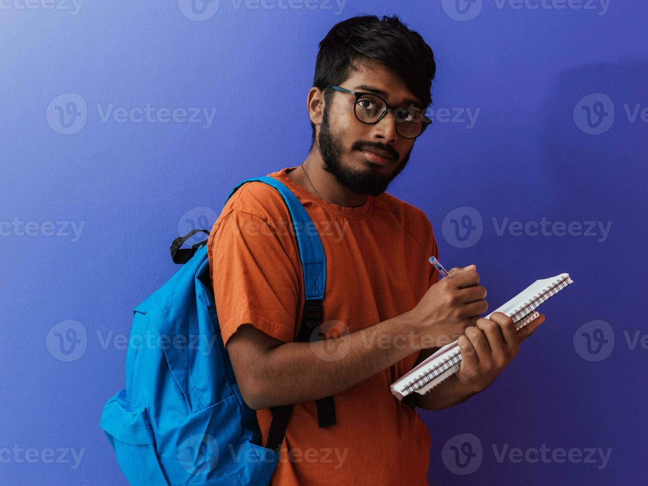 indisk studerande med blå ryggsäck, glasögon och anteckningsbok Framställ på lila bakgrund. de begrepp av utbildning och skolutbildning. tid till gå tillbaka till skola foto