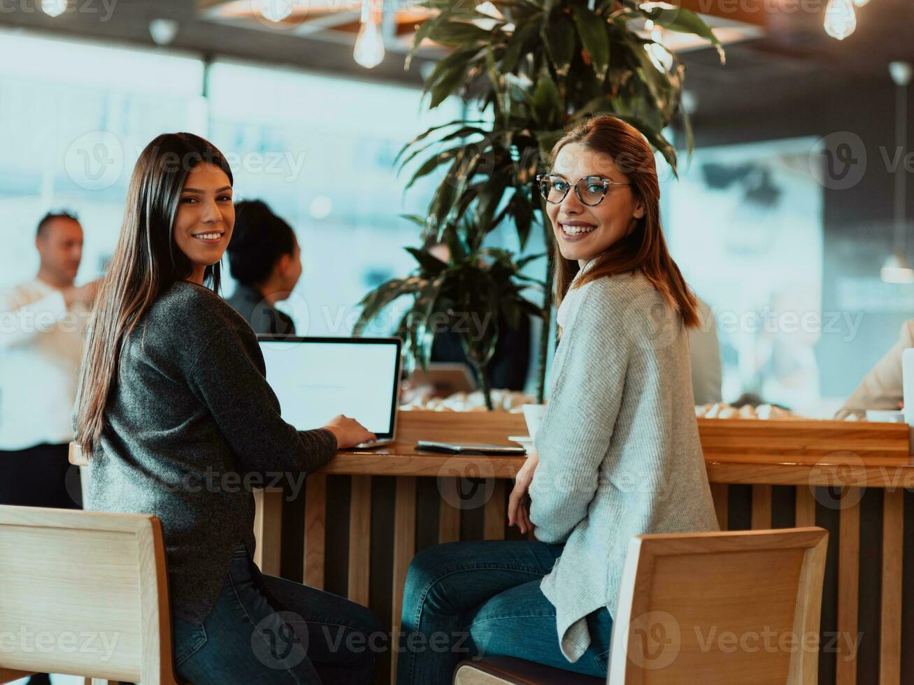 två ung företag kvinnor Sammanträde på tabell i Kafé. flicka visar kollega information på bärbar dator skärm. flicka använder sig av smartphone, bloggar. lagarbete, företag möte.. foto