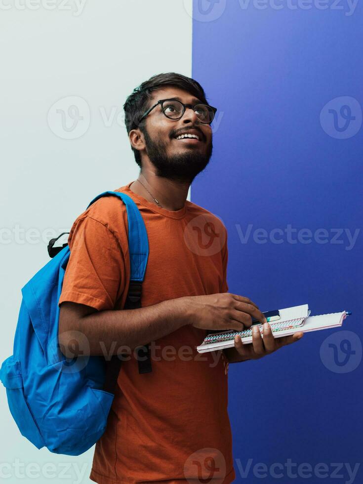 indisk studerande med blå ryggsäck, glasögon och anteckningsbok Framställ på de lila-grå bakgrund. de begrepp av utbildning och skolutbildning. tid till gå tillbaka till skola foto