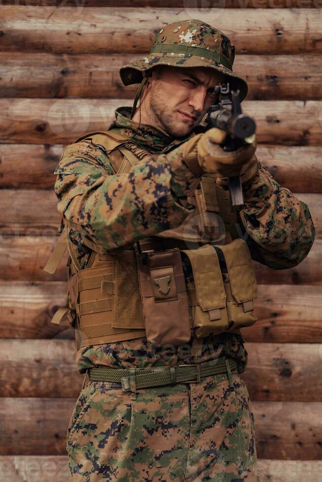 en soldat i enhetlig med en gevär i hans hand är stående i främre av en trä- vägg. en soldat vakter de skog bas från de fiende foto