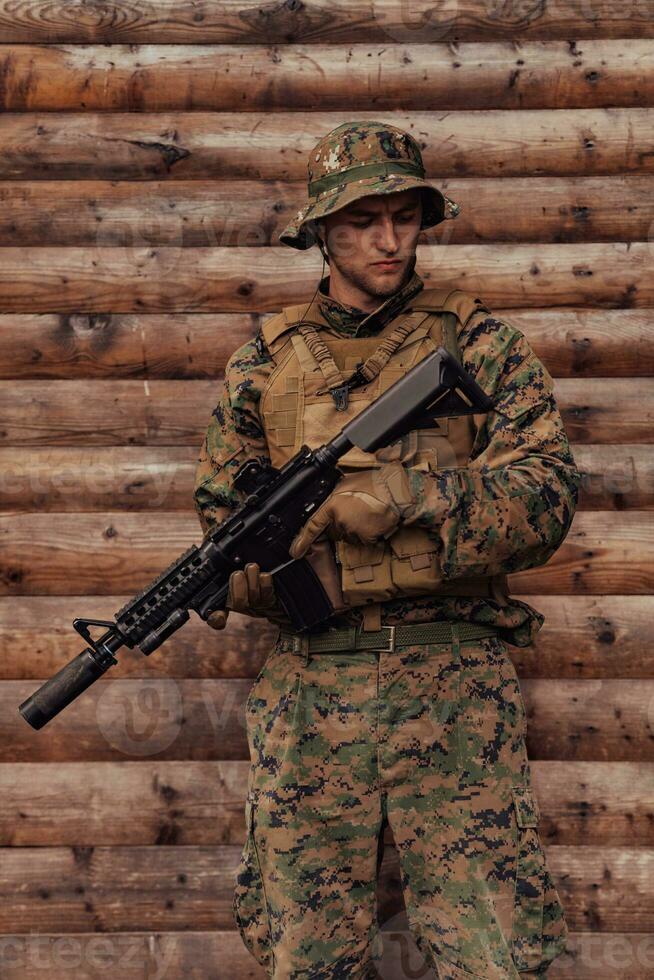 en soldat i enhetlig med en gevär i hans hand är stående i främre av en trä- vägg. en soldat vakter de skog bas från de fiende foto