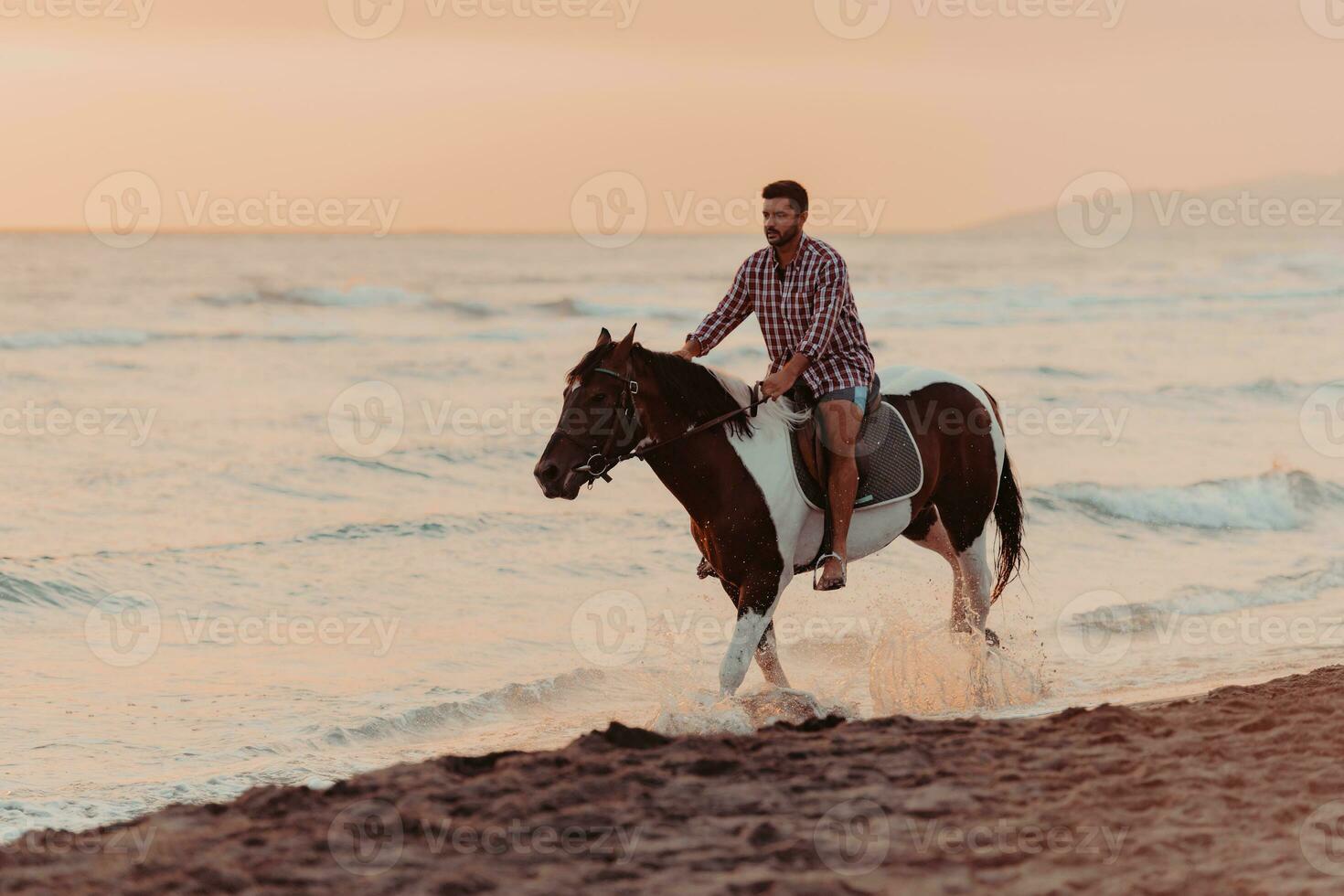 en modern man i sommar kläder åtnjuter ridning en häst på en skön sandig strand på solnedgång. selektiv fokus foto