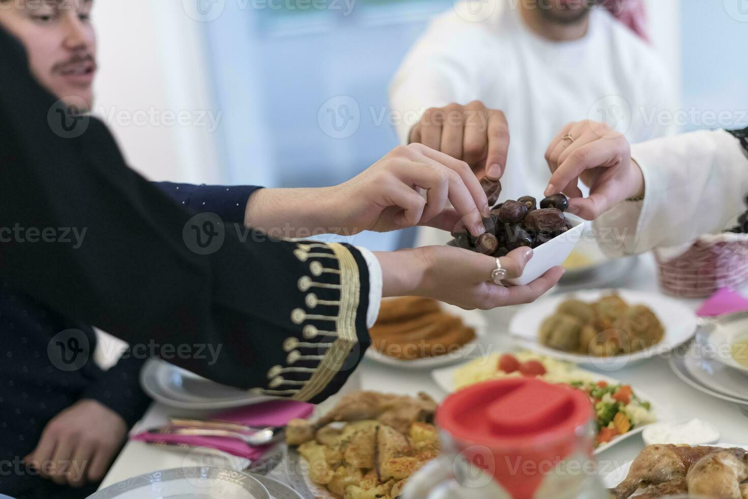 modern multietnisk muslim familj delning en skål av datum medan njuter iftar middag tillsammans under en ramadan fest på Hem foto