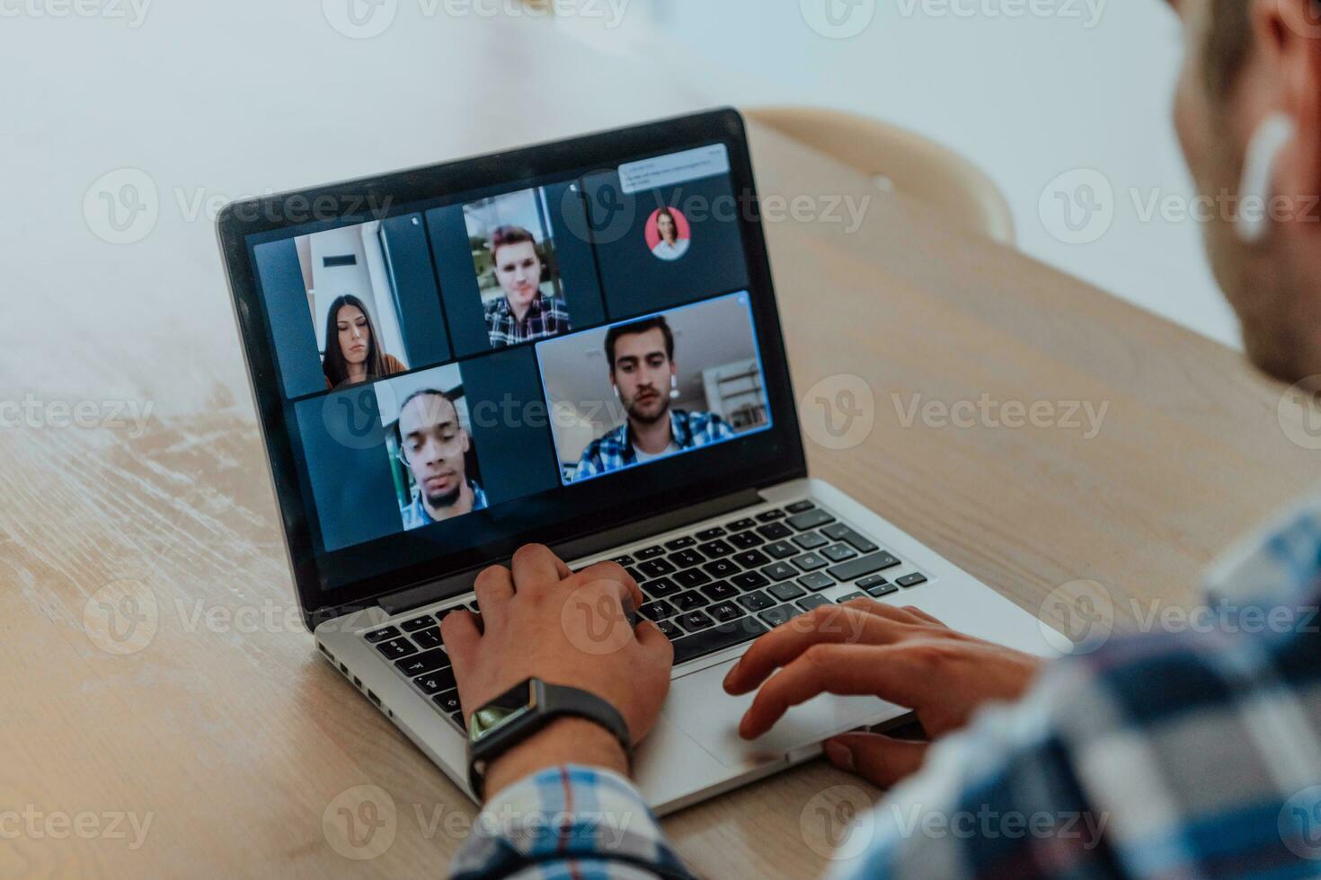 de man Sammanträde på en tabell i en modern levande rum, med hörlurar använder sig av en bärbar dator för företag video chatt, konversation med vänner och underhållning foto