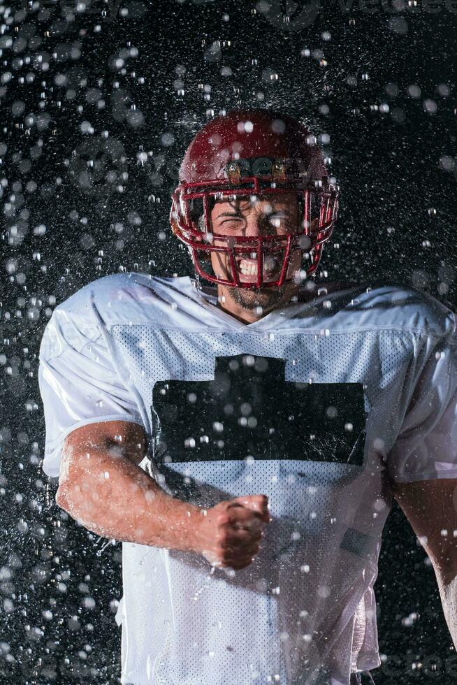 amerikan fotboll fält ensam idrottare krigare stående på en fält innehar hans hjälm och redo till spela. spelare framställning till springa, ge sig på och Göra landning. regnig natt med dramatisk dimma, blå ljus foto