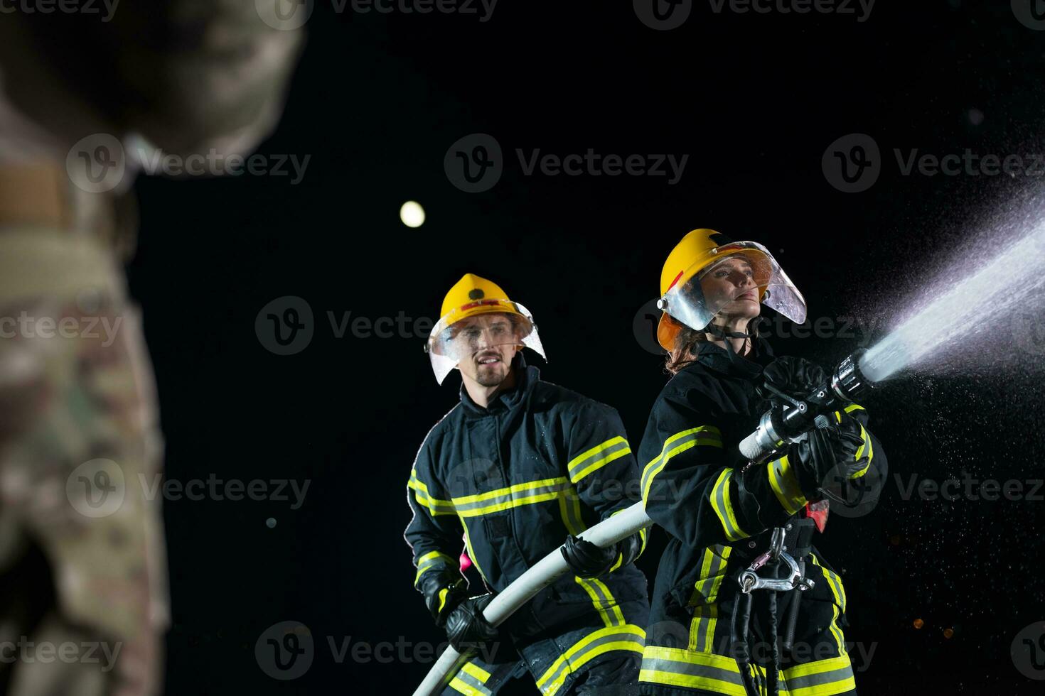 brandmän använder sig av en vatten slang till eliminera en brand fara. team av kvinna och manlig brandmän i farlig rädda uppdrag. foto