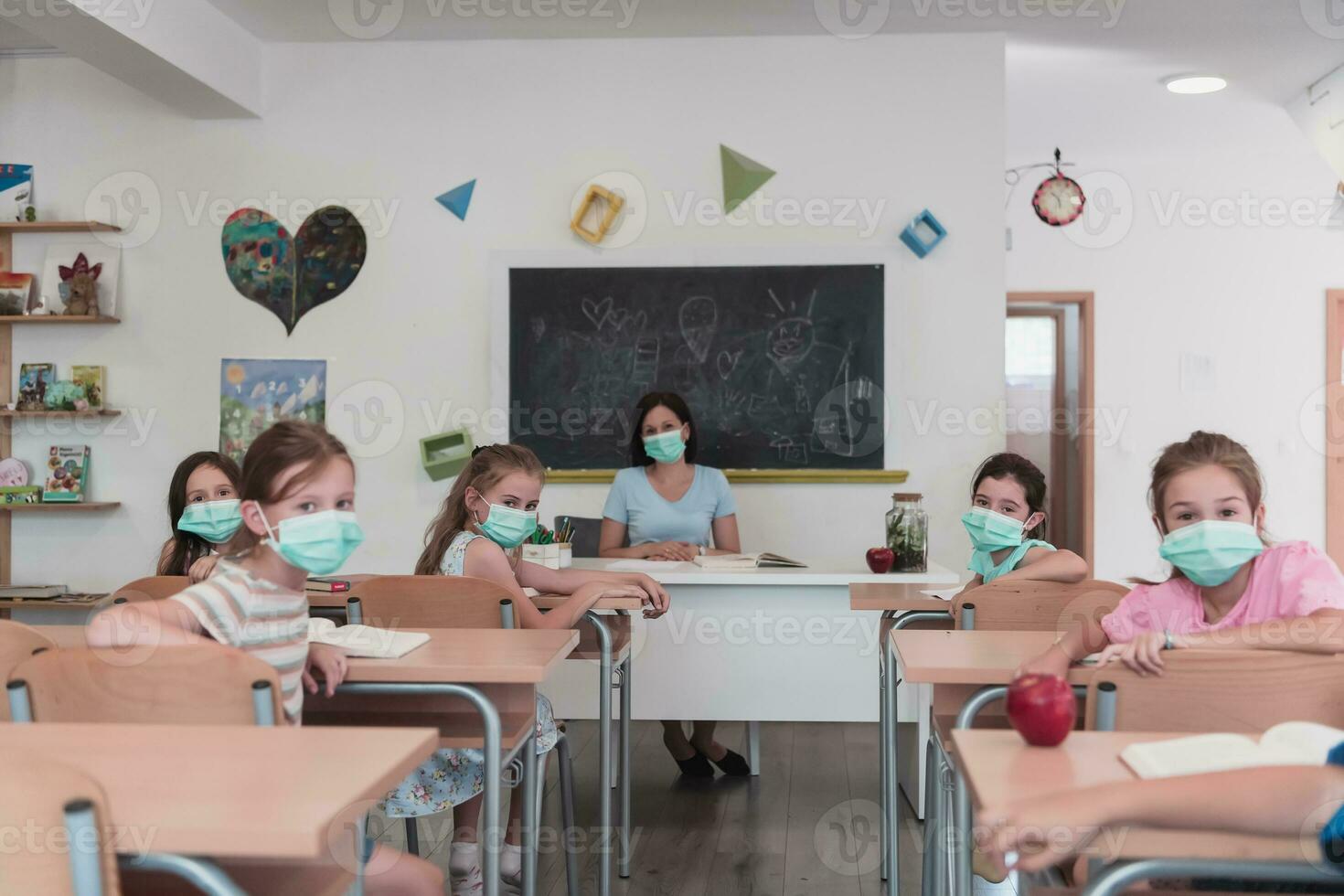 raser grupp av barn bär ansikte masker arbetssätt på klass, skrivning och lyssnande förklaringar av lärare i klassrum foto