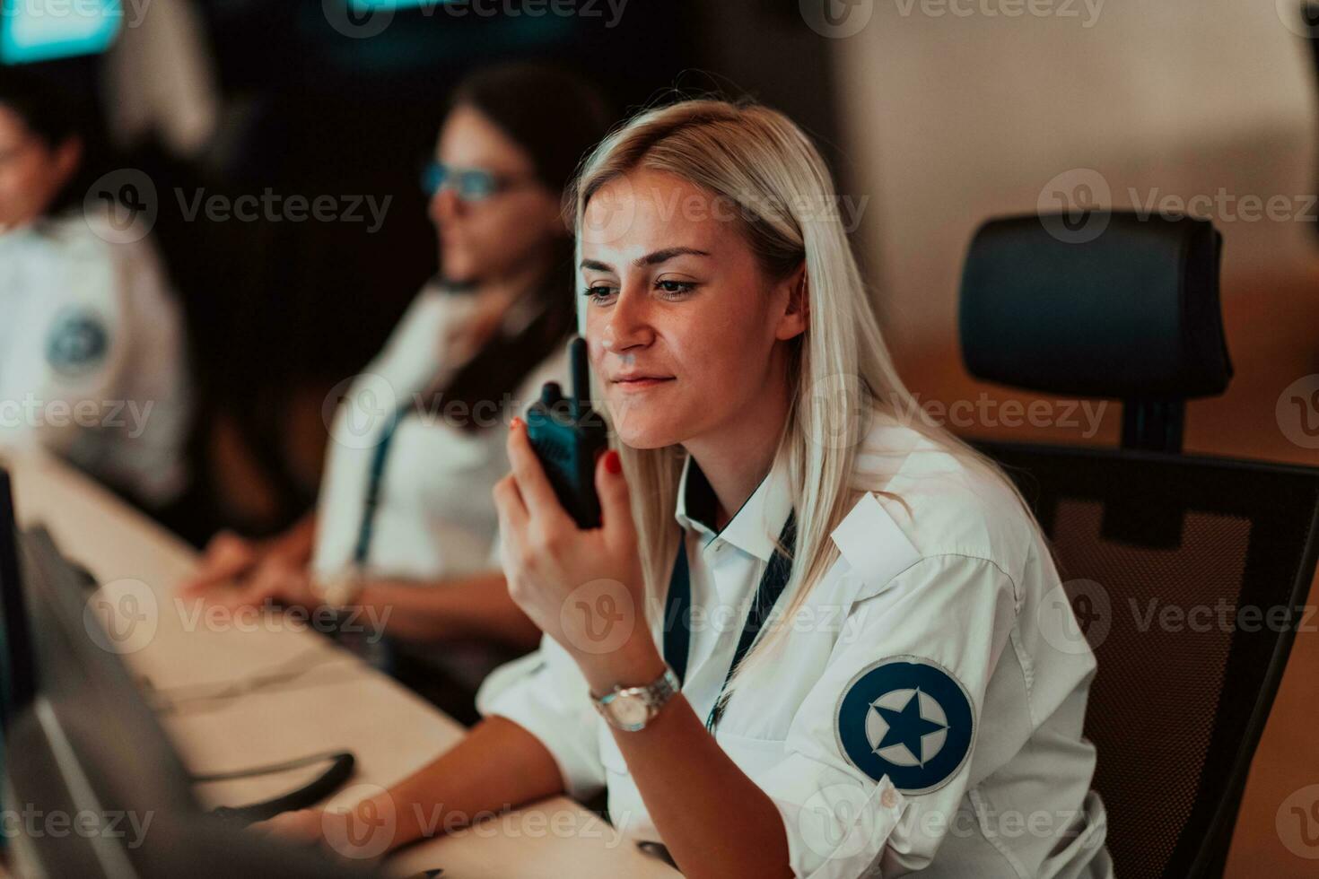 kvinna säkerhet operatör innehav bärbar radio i hand medan arbetssätt i en data systemet kontrollera rum kontor teknisk operatör arbetssätt på arbetsstation med flera olika skärmar, säkerhet vakt arbetssätt på foto