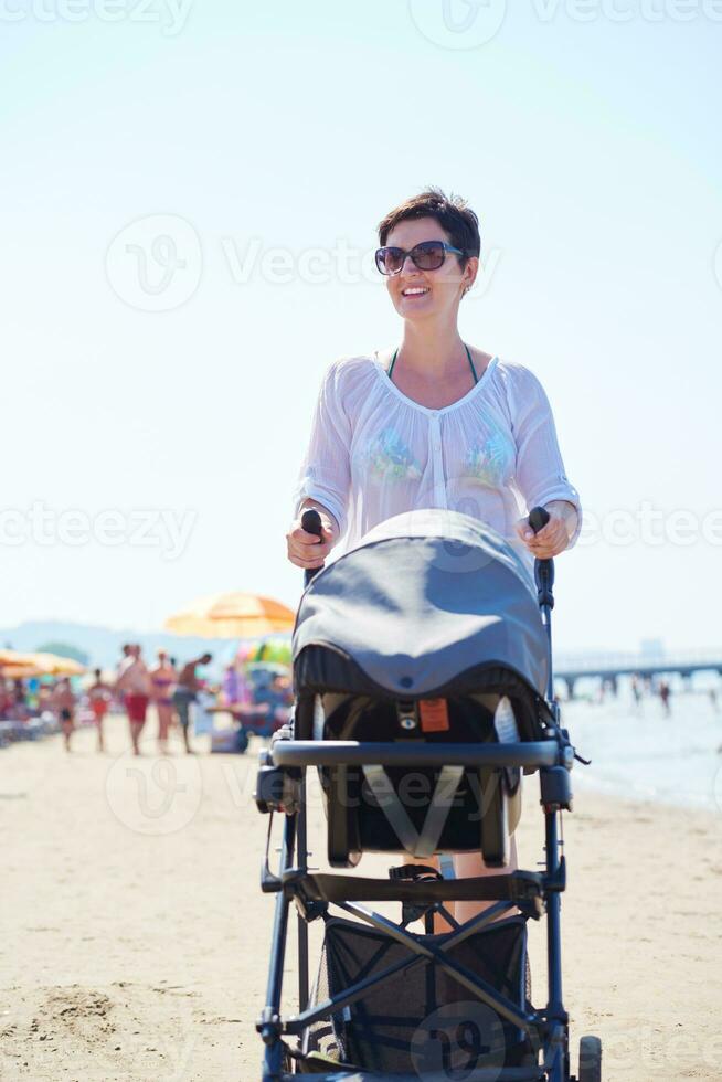 mor gående på strand och skjuta på bebis transport foto