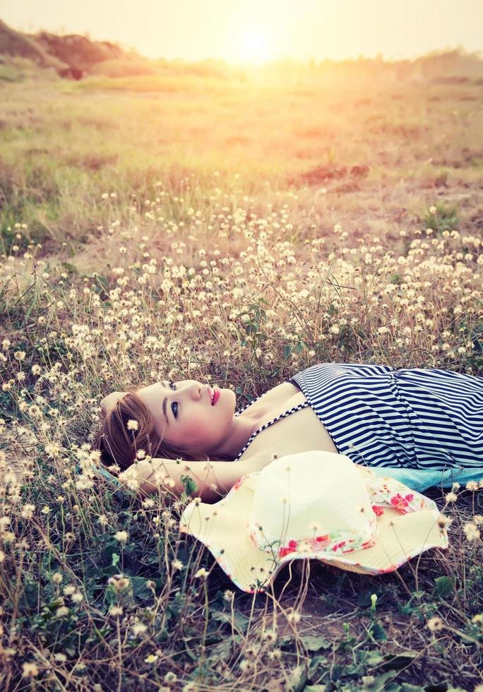 ung sexig kvinna som ligger i gräset och närmar sig hatten ser mot himlen. foto