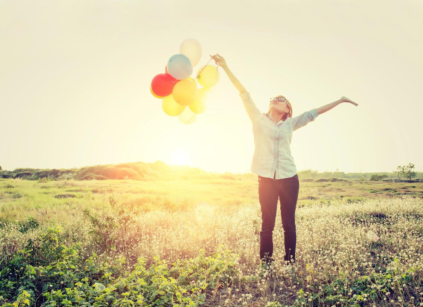 kvinna som står med ballonger i fältet och tittar in i himlen. foto