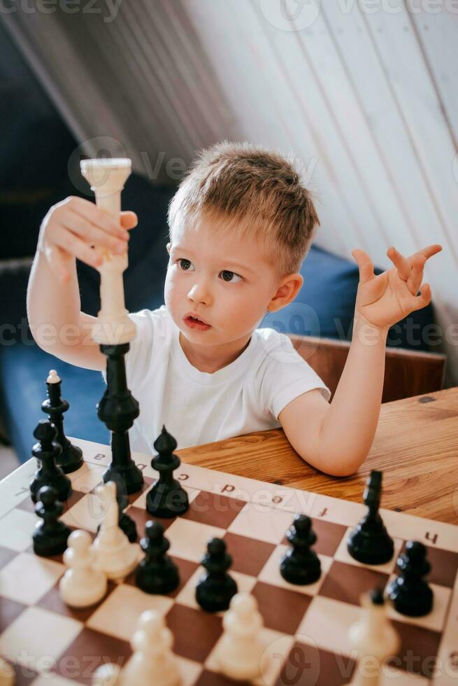 liten pojke spelar schack på Hem på de tabell foto