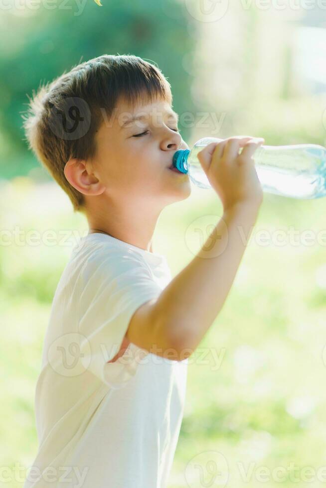 söt barn drycker vatten från en flaska på de gata i sommar foto