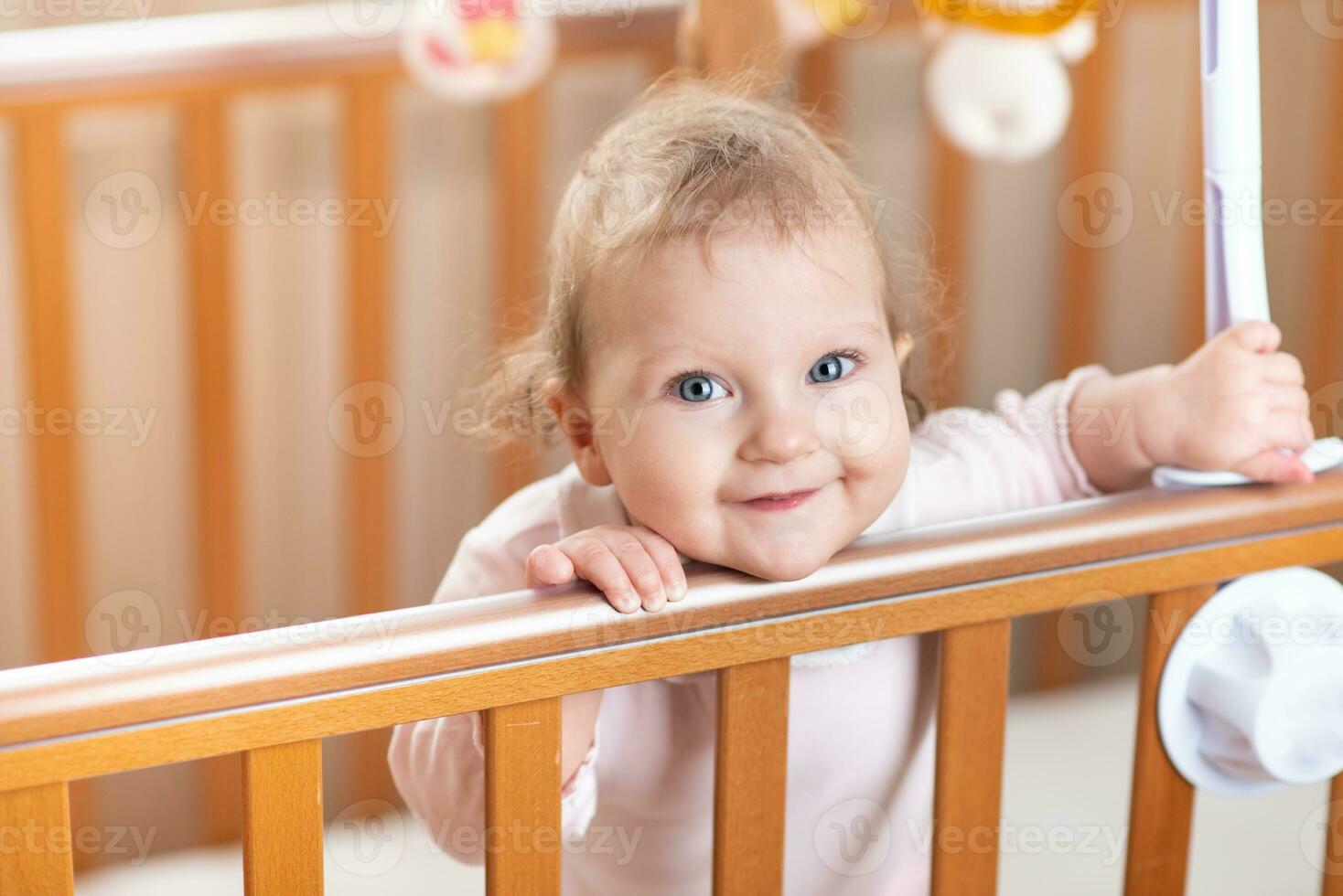 porträtt av en skrattande bebis vem är stående i en spjälsäng foto
