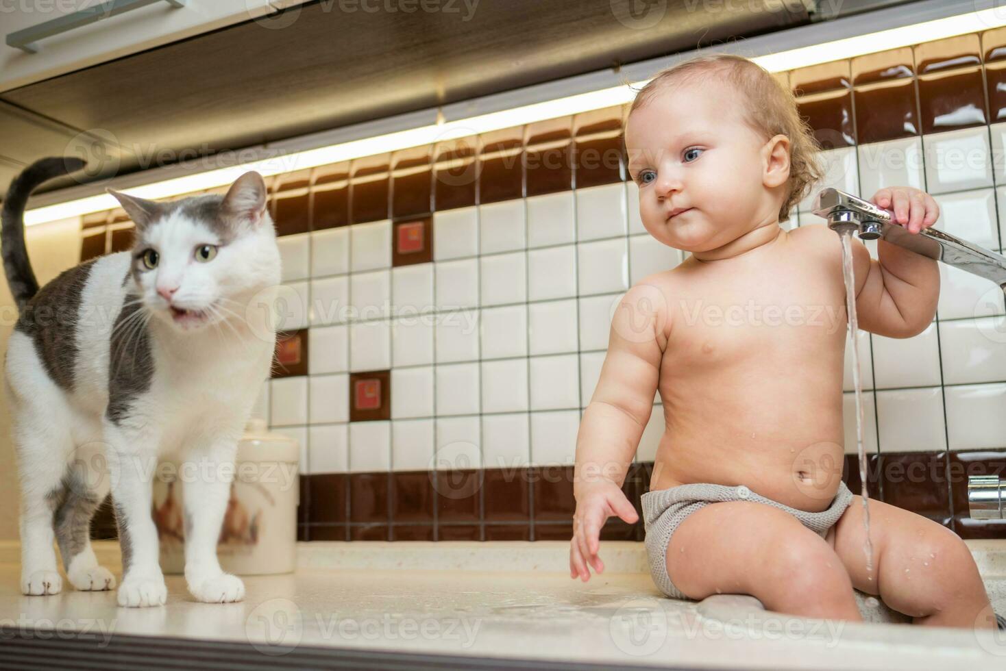 söt bebis spelar i de kök handfat med en katt foto