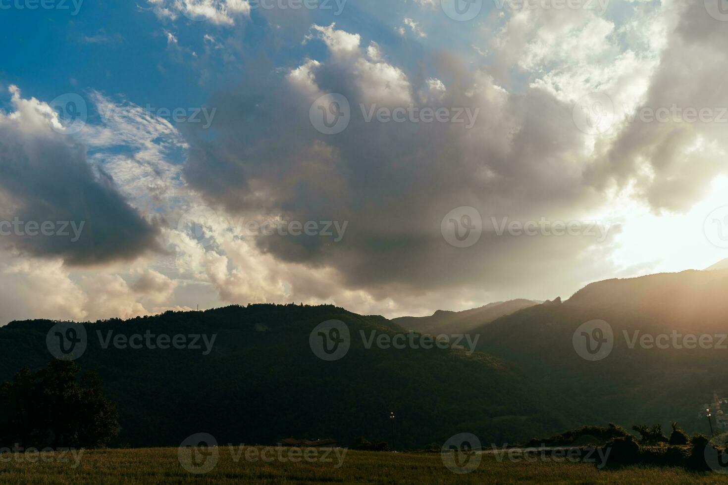 panorama- se av en dal omgiven förbi kullar på solnedgång med de Sol dolt förbi moln foto