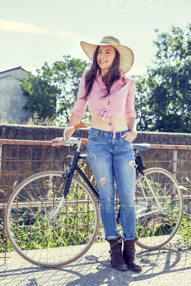 Söt ung kvinna på cykel i en Land väg foto