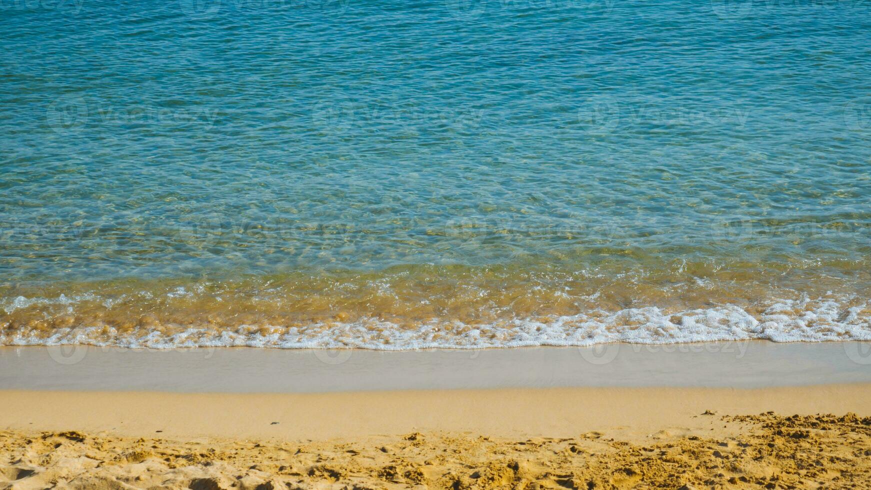 sandig strand med små vågor - blå hav och gul sand foto