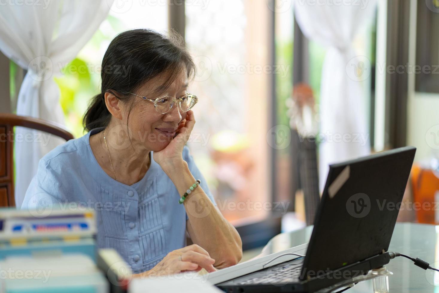 senior asiatisk woamn använder datorn för att skicka e -post till vän hemma foto