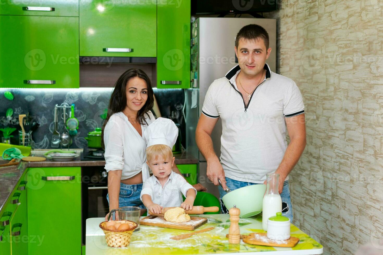 Lycklig familj mamma och liten son och pappa är framställning deg i kök på tabell. Produkter för deg är på tabell foto