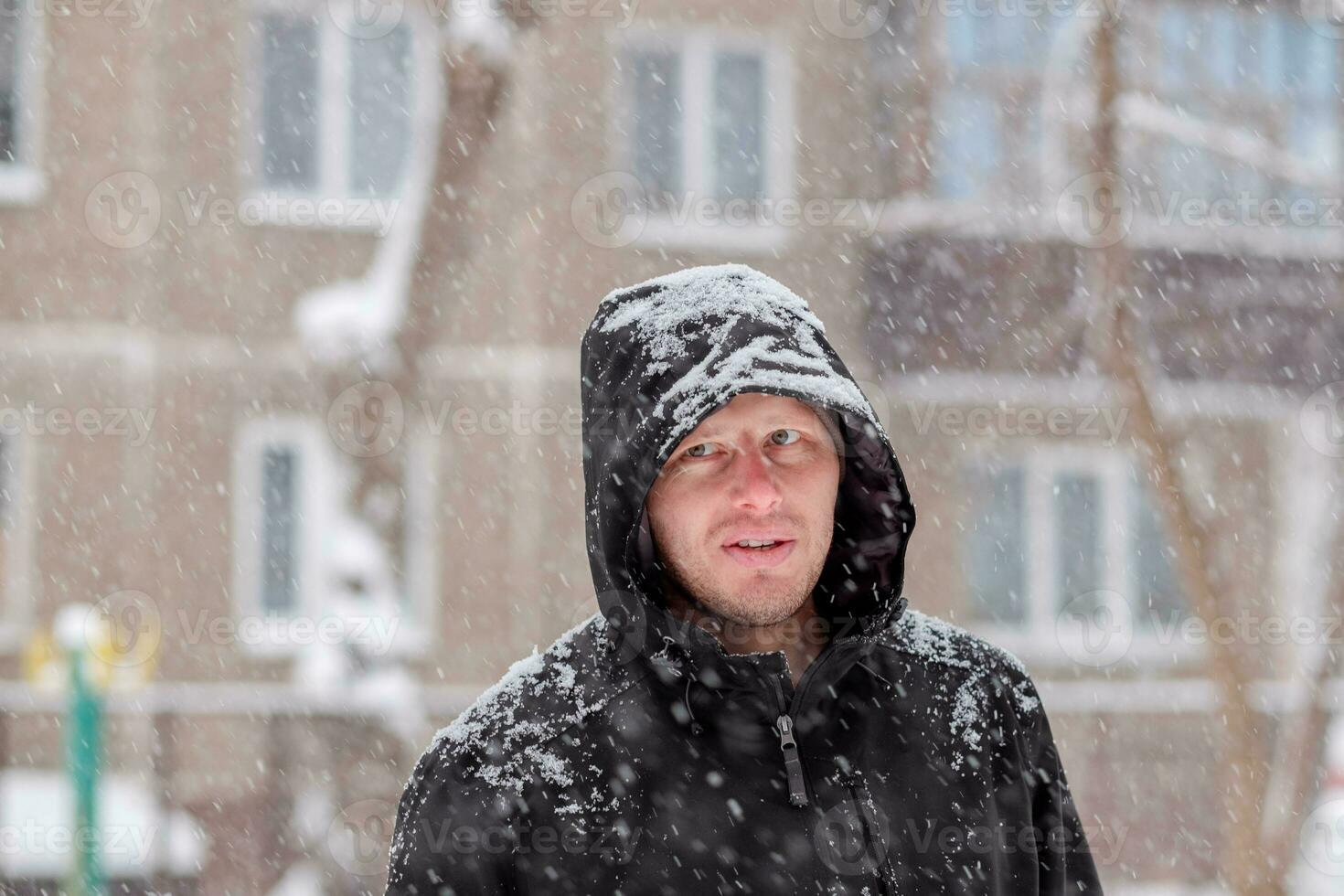 man i en huva under en snöfall. porträtt av en man i vinter. allvarlig se foto