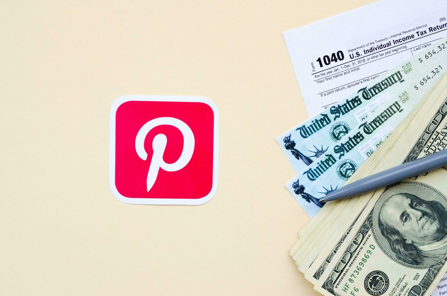 Pinterest tryckt logotyp lögner med 1040 enskild inkomst beskatta lämna tillbaka form med återbetalning kolla upp och hundra dollar räkningar på beige bakgrund. hjälp i beskatta period från social nätverk begrepp foto