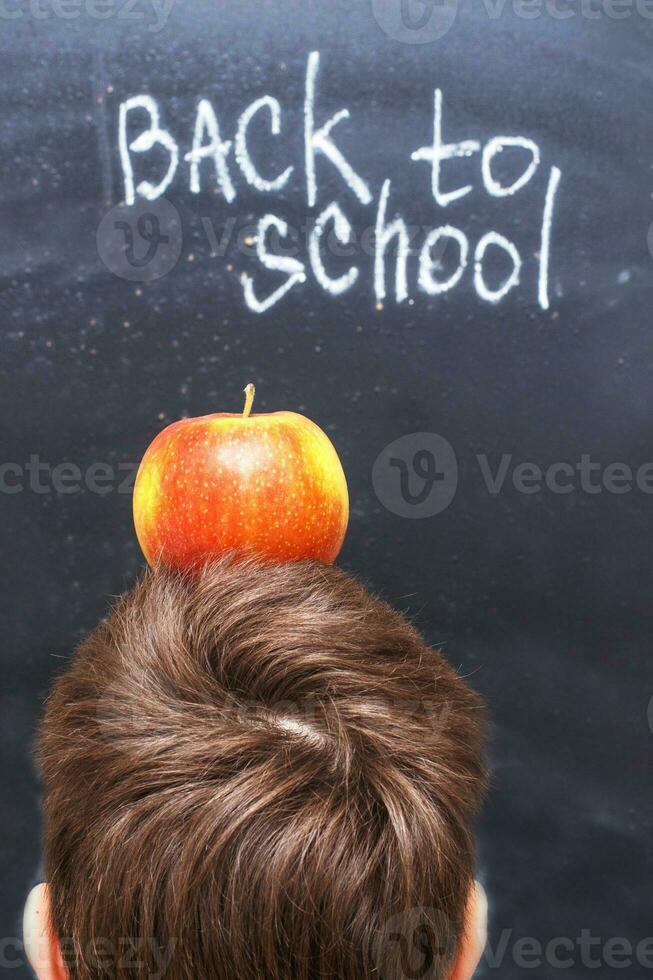 ett äpple på en barnets huvud nära svarta tavlan. tillbaka till skola begrepp bakgrund foto