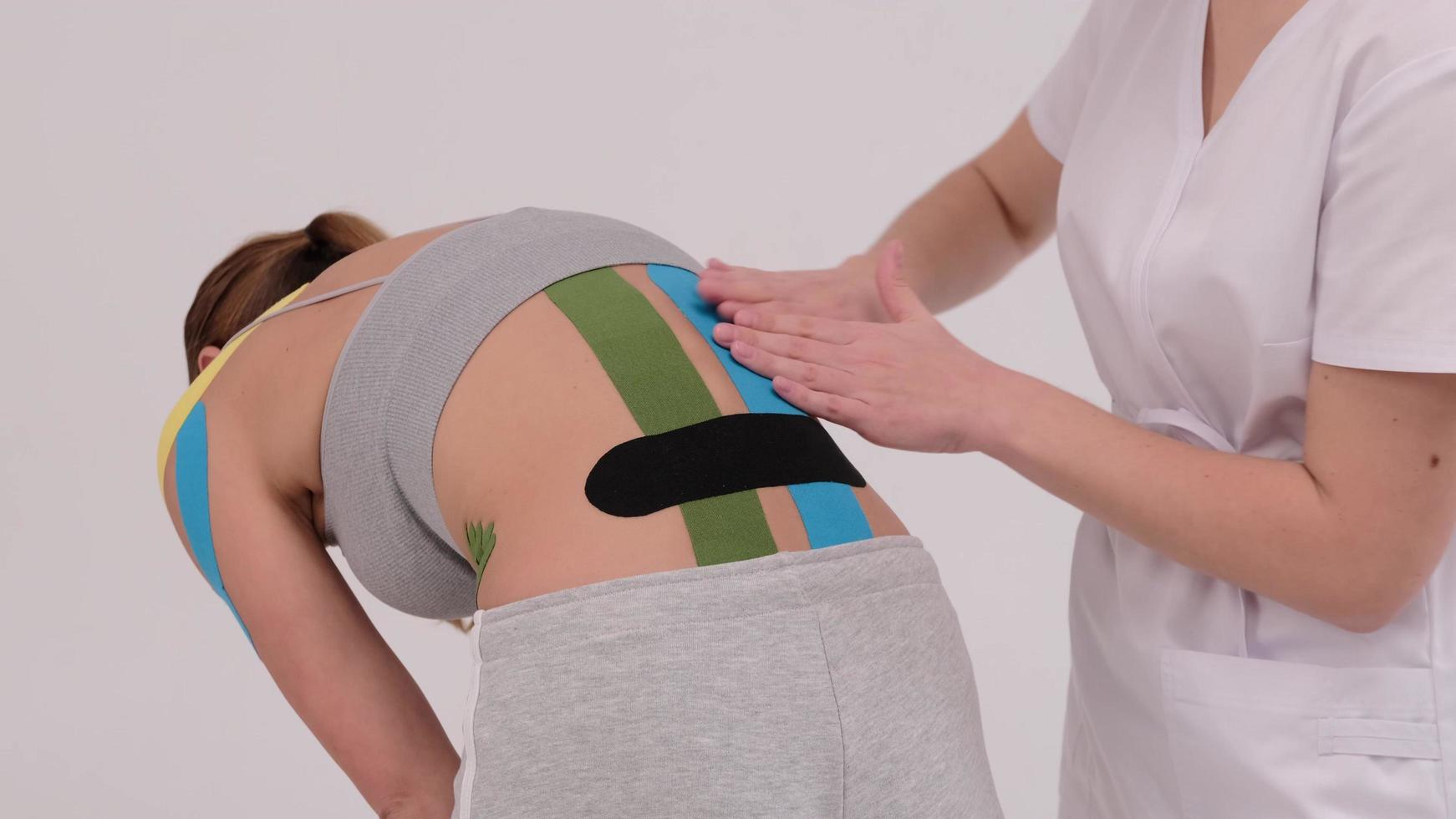 demonstrationsvideo av en terapeut som tejper kinesiotejp på en kvinnlig patient tillbaka. smärtbehandling. sport och rehabilitering foto