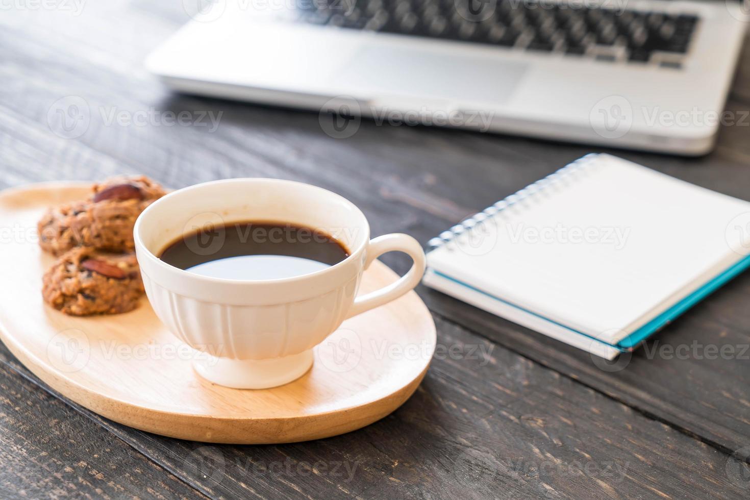 svart kaffe och kakor med bärbar dator och anteckningsbok på bordet foto