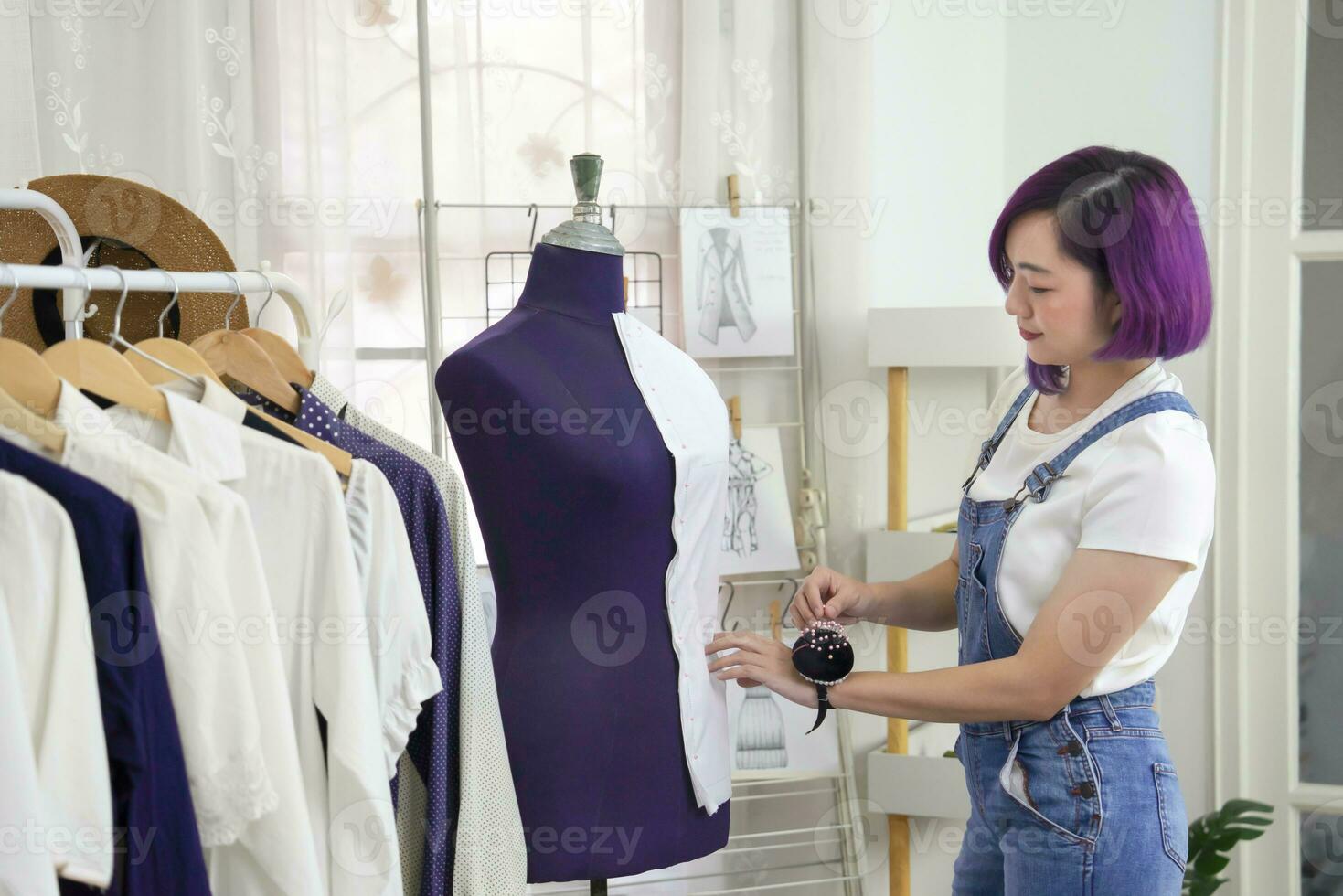 ung asiatisk kvinna Kläder designer arbetssätt med mannekäng på mode studio, koncept av mode design och skrädderi företag foto
