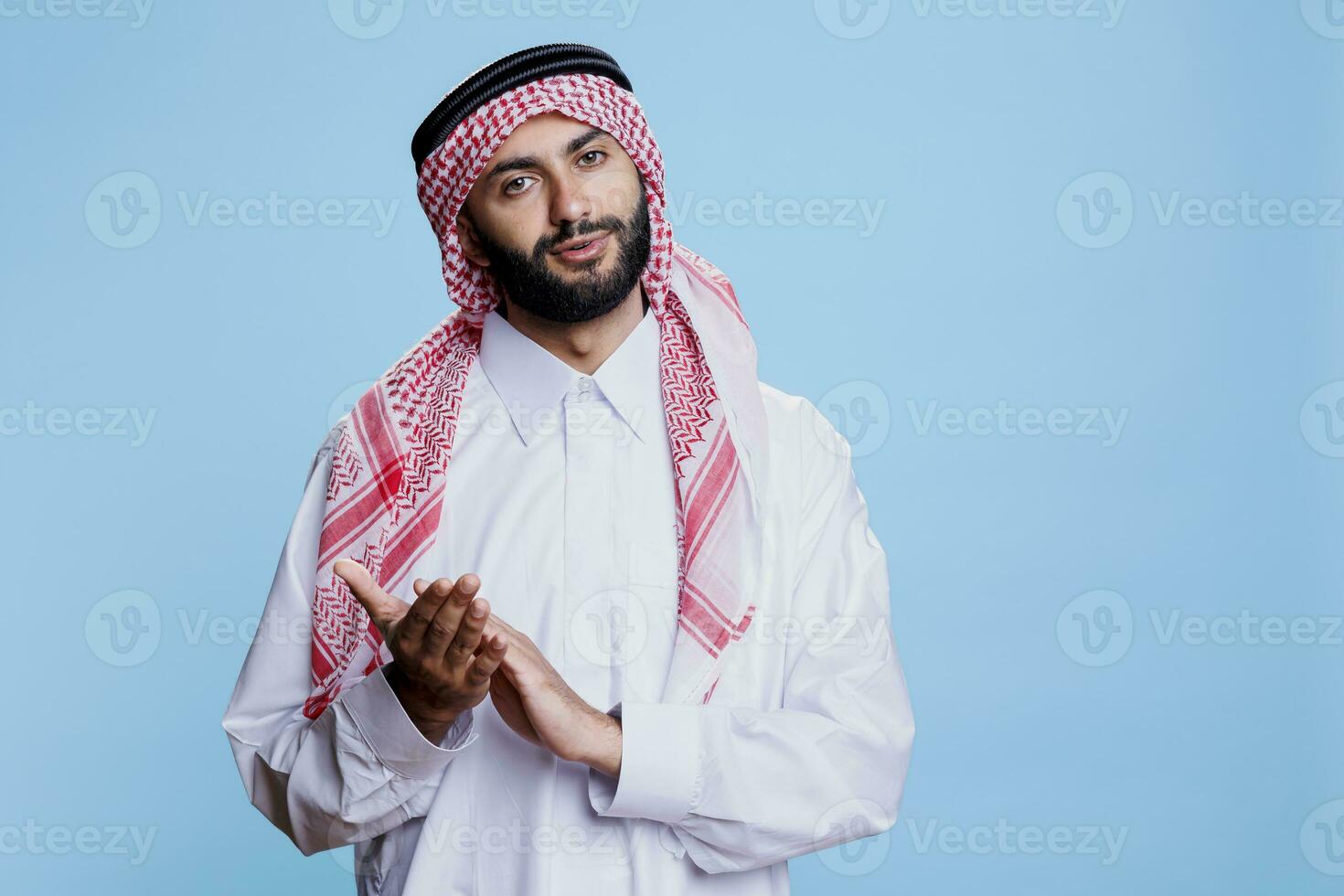 arab man klädd i traditionell islamic kläder framställning applåder, gratulera och ser på kamera med självsäker uttryck. muslim person bär thobe applåderar studio porträtt foto