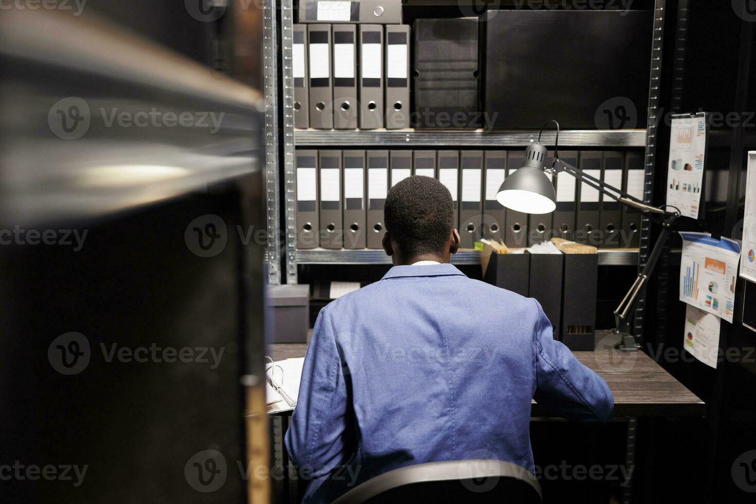 bokhållare Sammanträde på skrivbord i lagring rum, arbetssätt på byråkrati spela in, läsning filer med administrativ Rapportera. afrikansk amerikan chef analyserar bokföring dokument i företags- depositarie foto