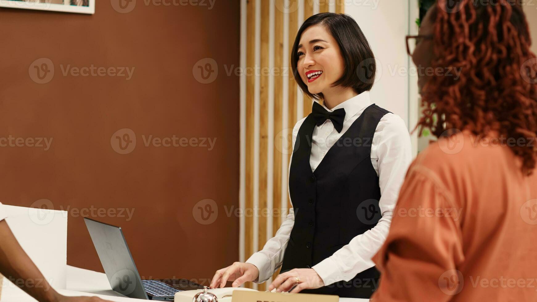 Lycklig vänlig asiatisk receptionist portion gäster under kolla upp i bearbeta, imputerande deras personlig information på bärbar dator. turister bokning i deras stanna kvar i lyx hotell, assisterad förbi hotell personal foto