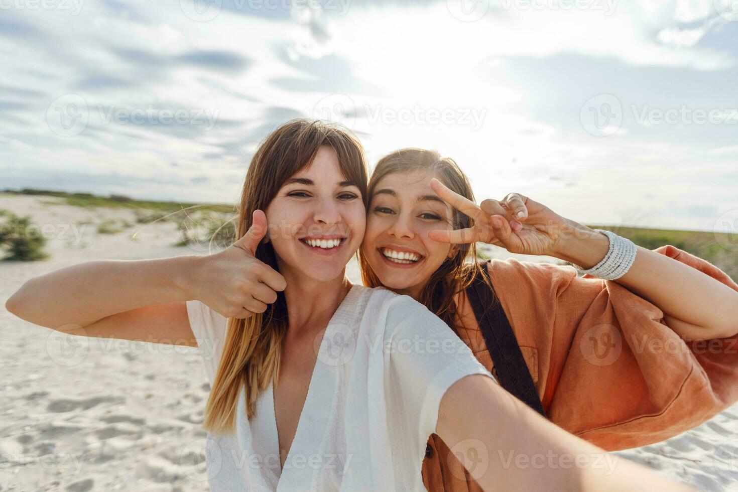 två kvinnor leende och Framställ för de kamera på de strand foto