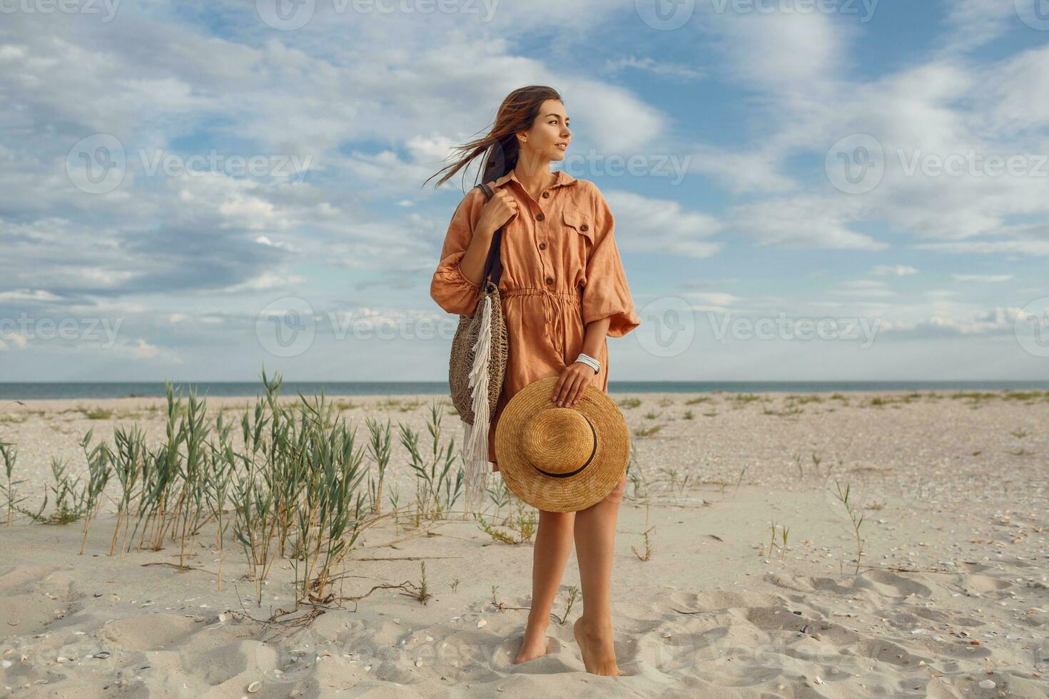 en kvinna i ett orange klänning och hatt på de strand foto