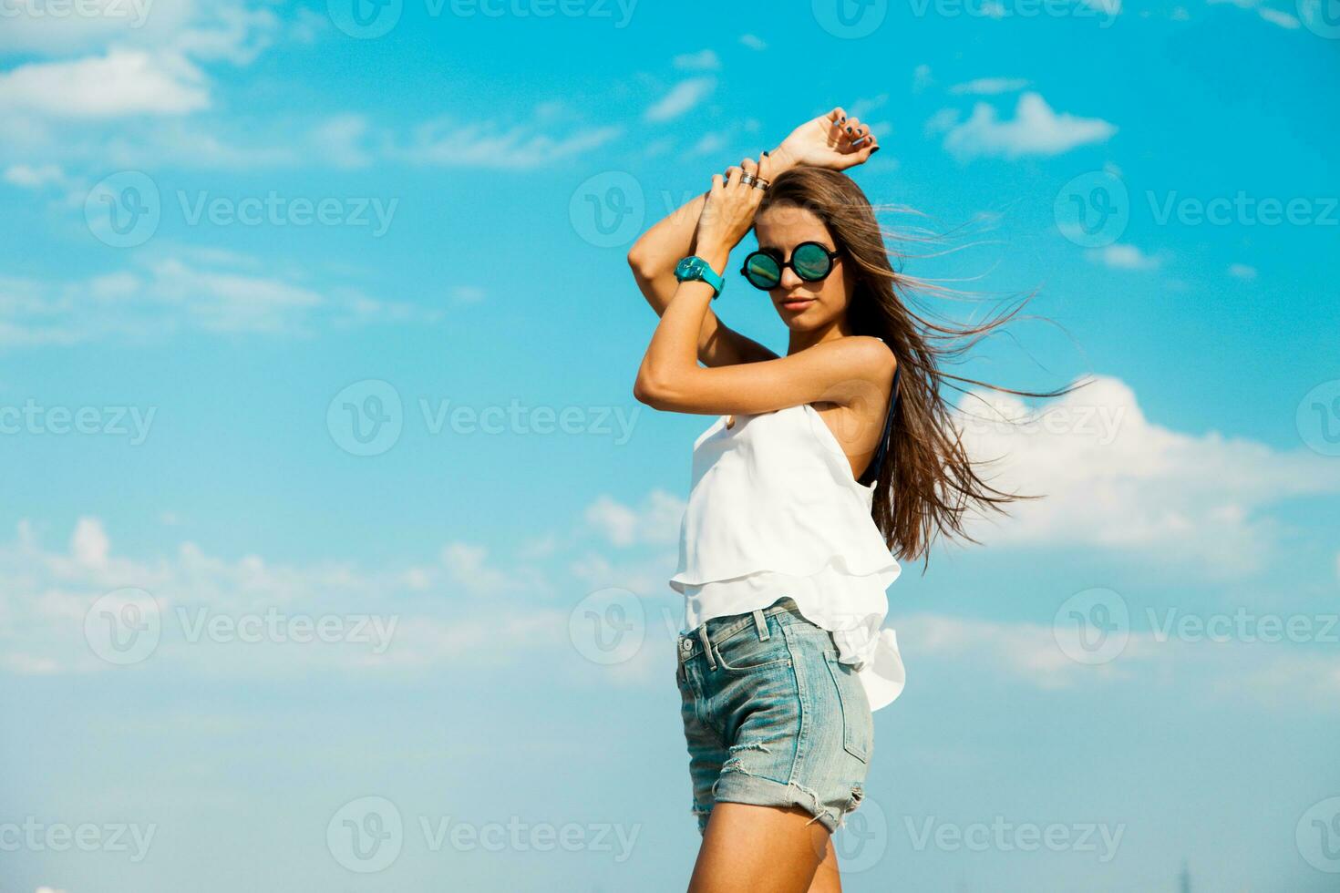 kvinna i vit t skjorta och eleganta solglasögon Framställ på de strand. blå himmel. foto