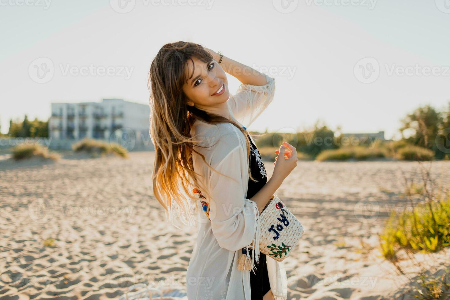 charmig flicka med vågig brunett hårstrån, klädd i vit boho omslag upp, gående på sommar strand. foto
