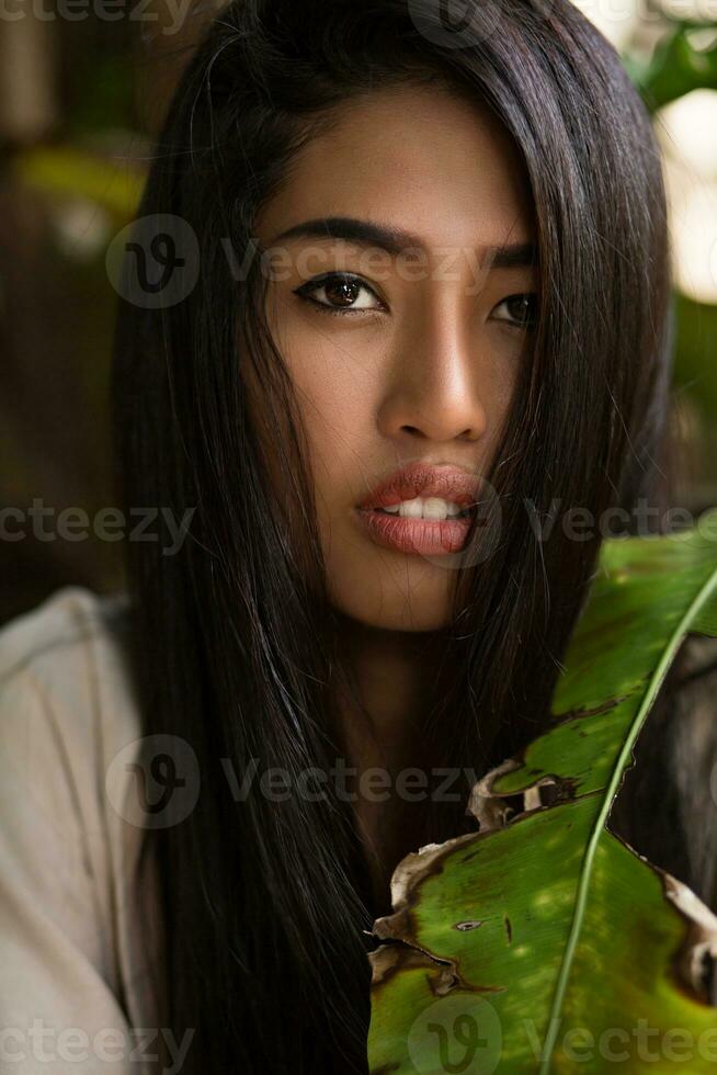 stänga upp skönhet porträtt av asiatisk kvinna med perfekt hud Framställ i tropisk trädgård. foto