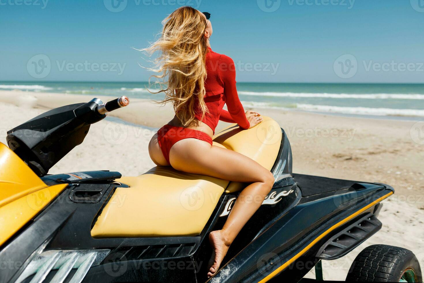 se från tillbaka av sexig solbränd kvinna bikini modell på tropisk sand strand. glamour flicka i baddräkt på de vatten skoter. foto