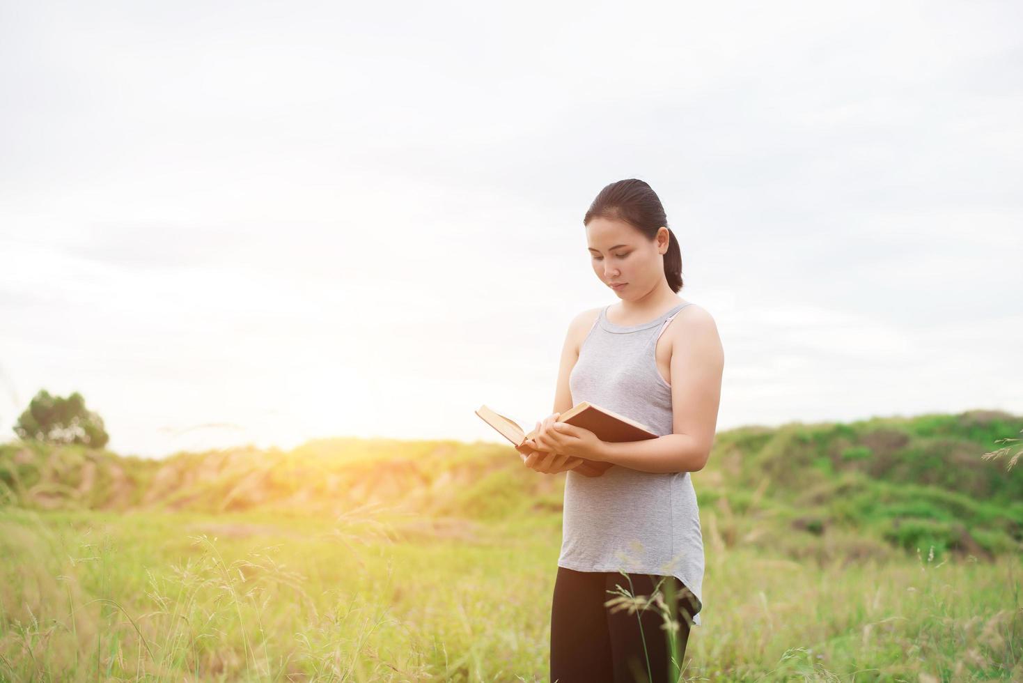ung kvinna som står och läser en bok på ängar foto