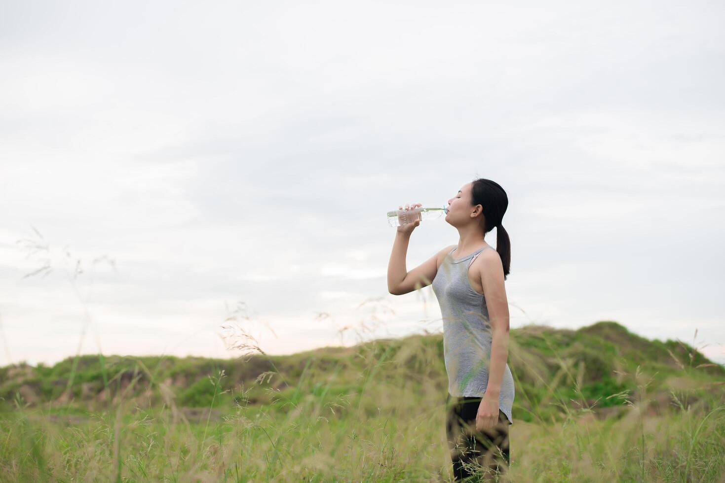 vacker ung kvinna som dricker vatten efter träning yoga på ängar foto